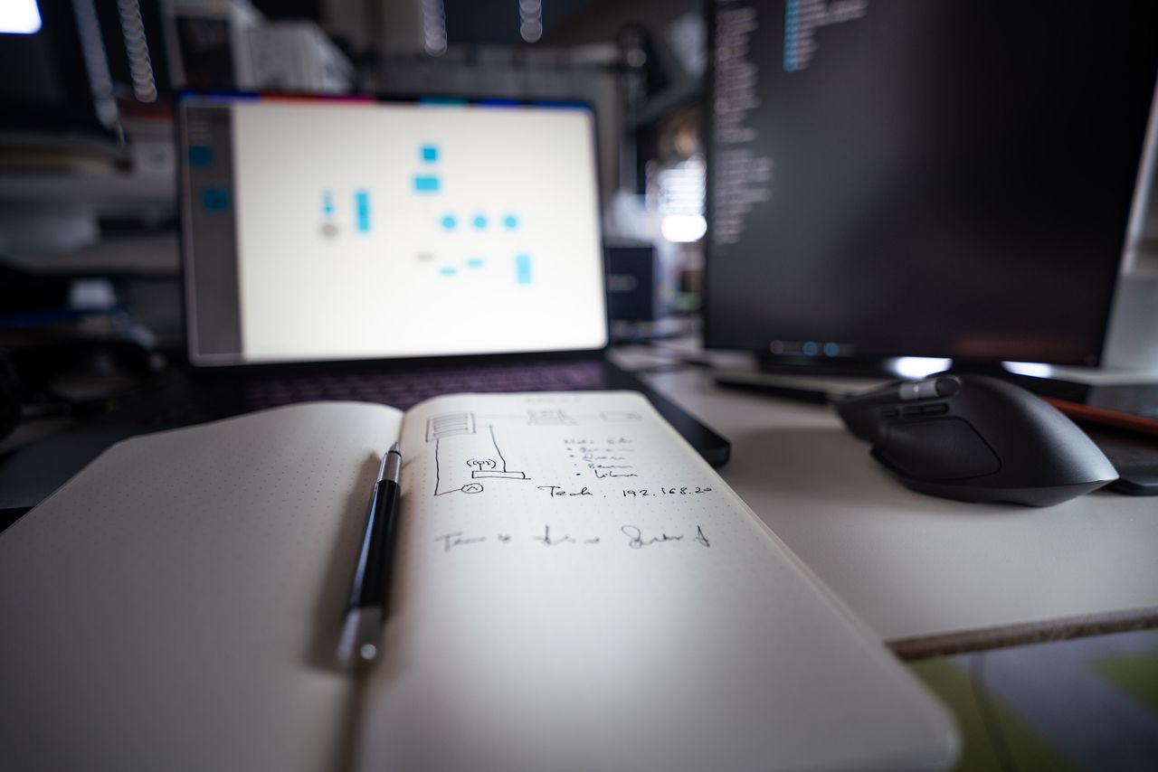 Close-up of a modern desk setup featuring notebooks, monitors, and a computer mouse.